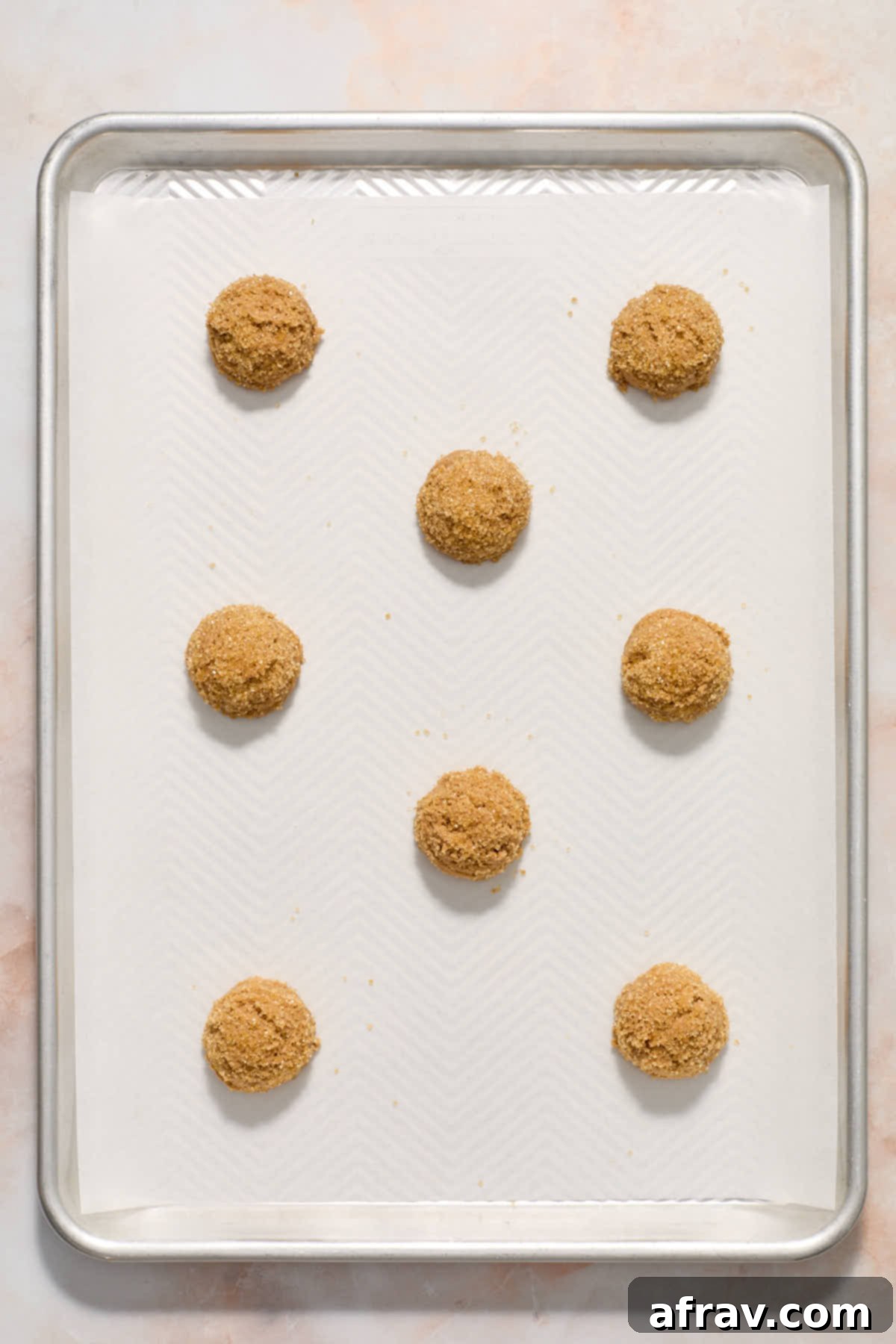 Scooped cookie dough balls, some with chocolate chips pressed into the top, arranged on a parchment-lined baking sheet.