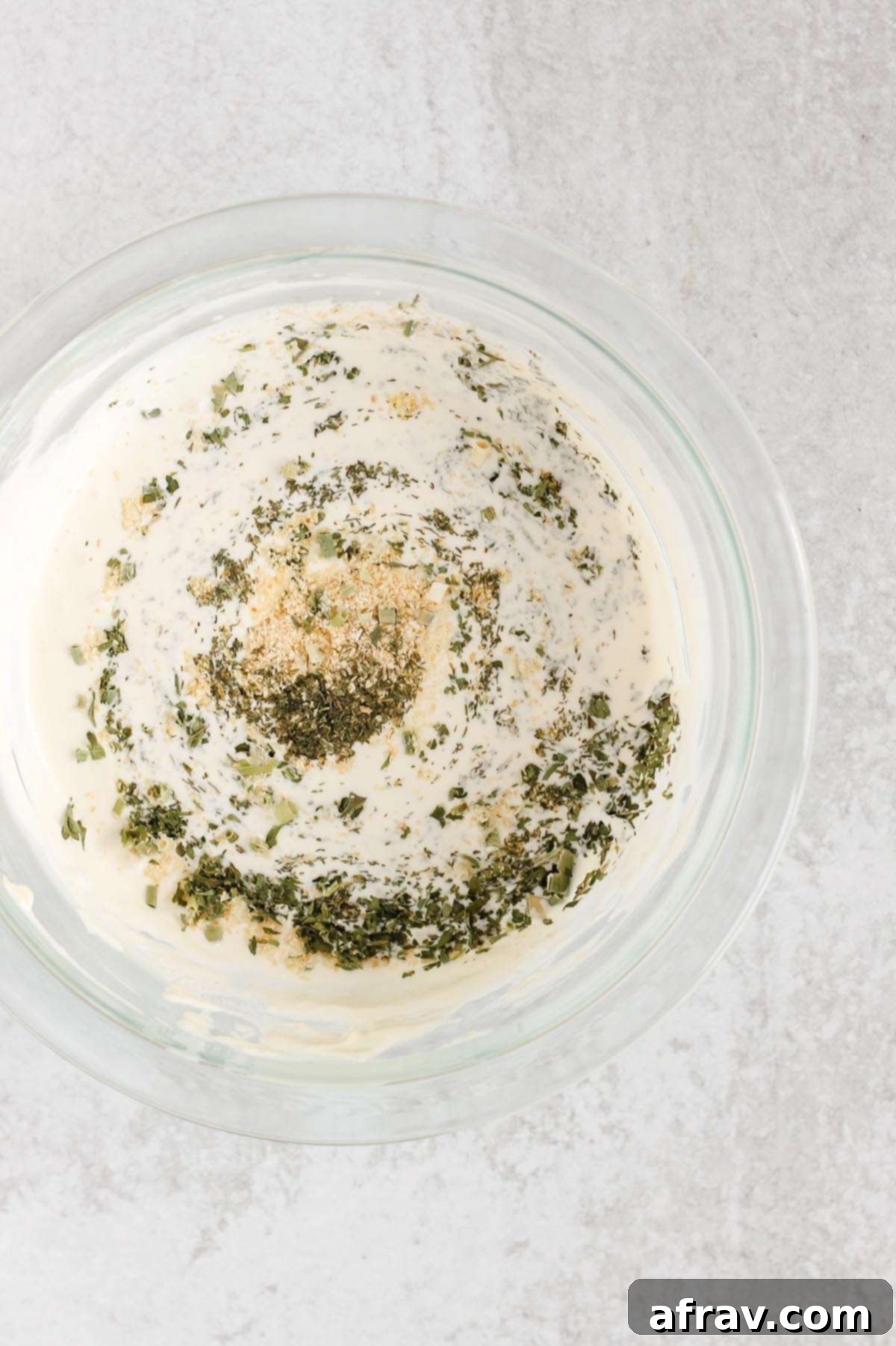 Effortless Dairy-Free Paleo Ranch Dressing 4 Mayonnaise, yogurt, and herbs being mixed in a mixing bowl for homemade dairy-free ranch.