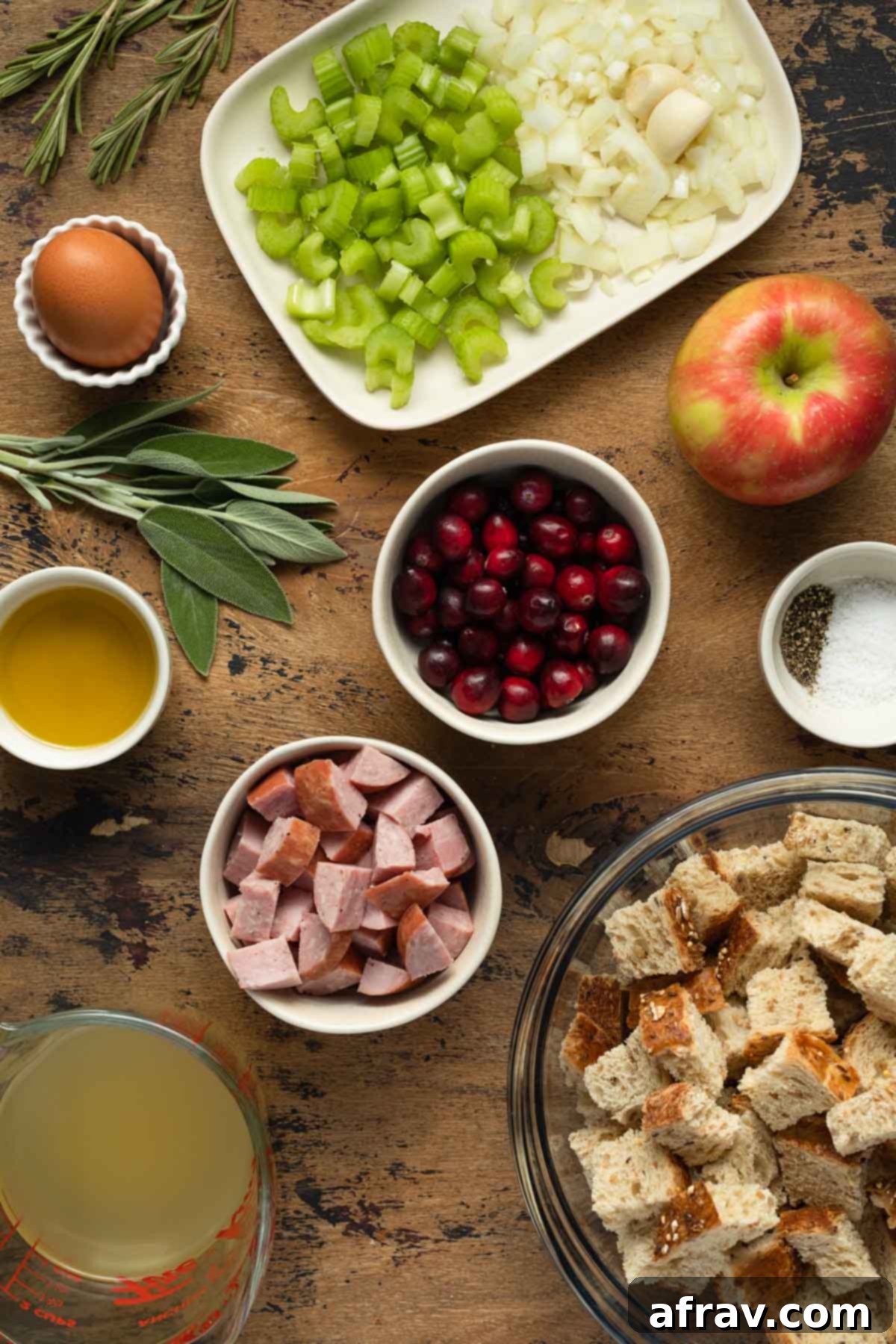 Ingredients to make whole wheat stuffing, including bread cubes, sausage, cranberries, and herbs, arranged individually on a rustic wooden surface for a perfect holiday recipe.