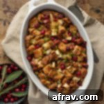 Whole wheat stuffing in a white baking dish with cranberries and sage off to the side, ready for a festive holiday meal.