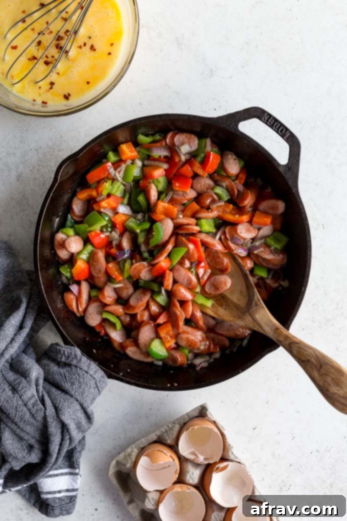 Sausage, peppers and onions in a cast iron skillet with the egg mixture off to the side.
