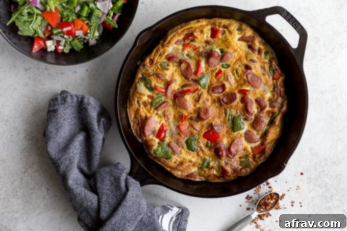 Sausage frittata with peppers and onions in a cast iron skillet with a cloth around the handle.