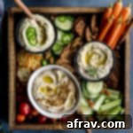 White bean dips arranged in a wooden tray with crackers and veggies for dipping.