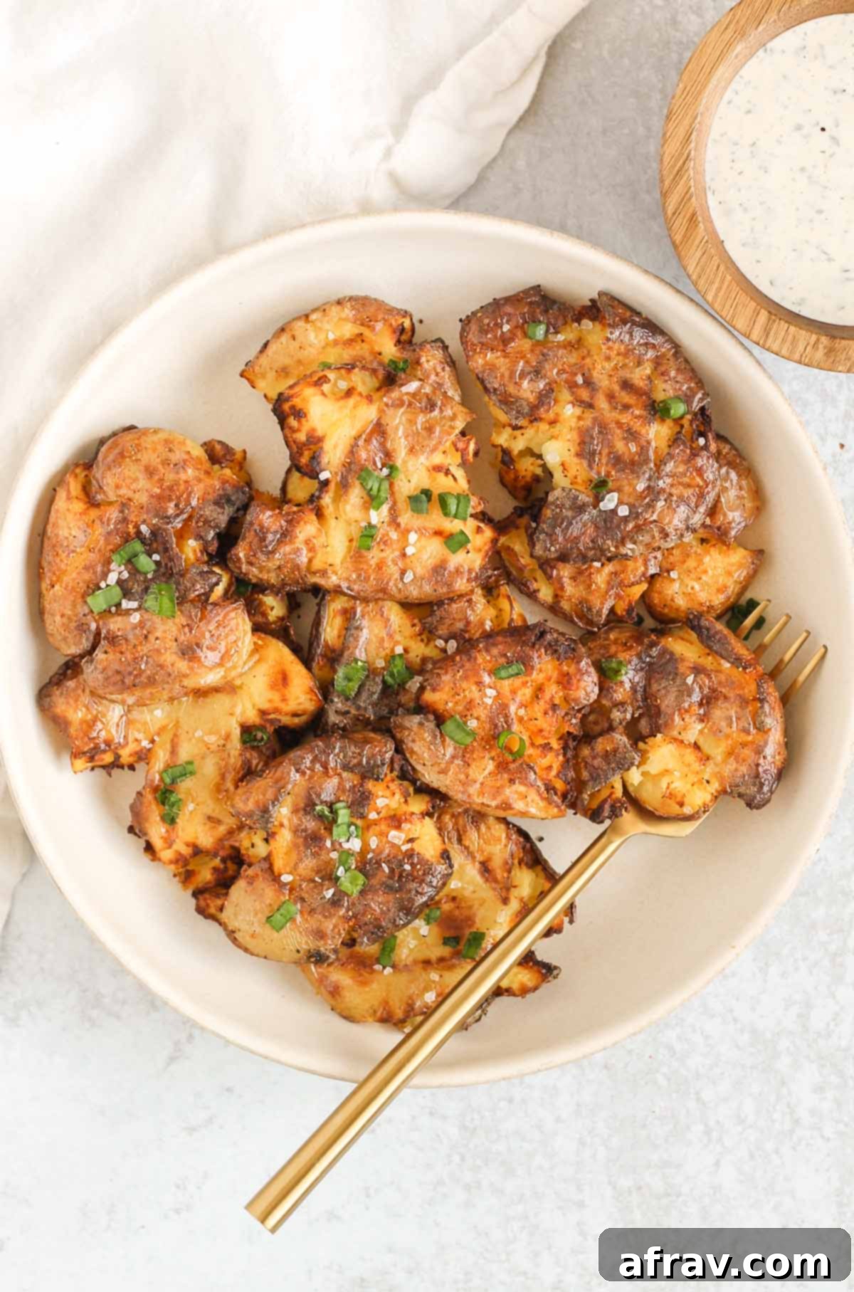 Smashed potatoes with a gold fork on a serving plate.