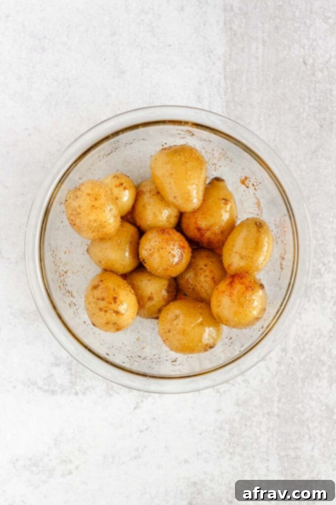 Potatoes tossed in olive oil and seasoning in a mixing bowl.