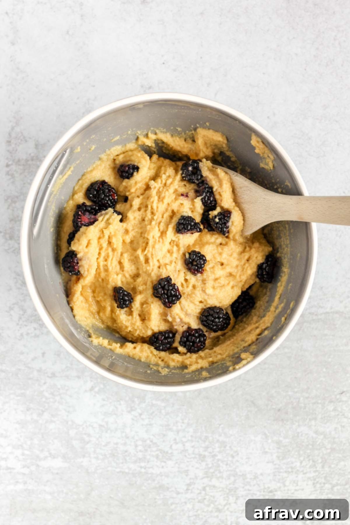 Wooden spoon folding blackberries into almond batter muffin mix.