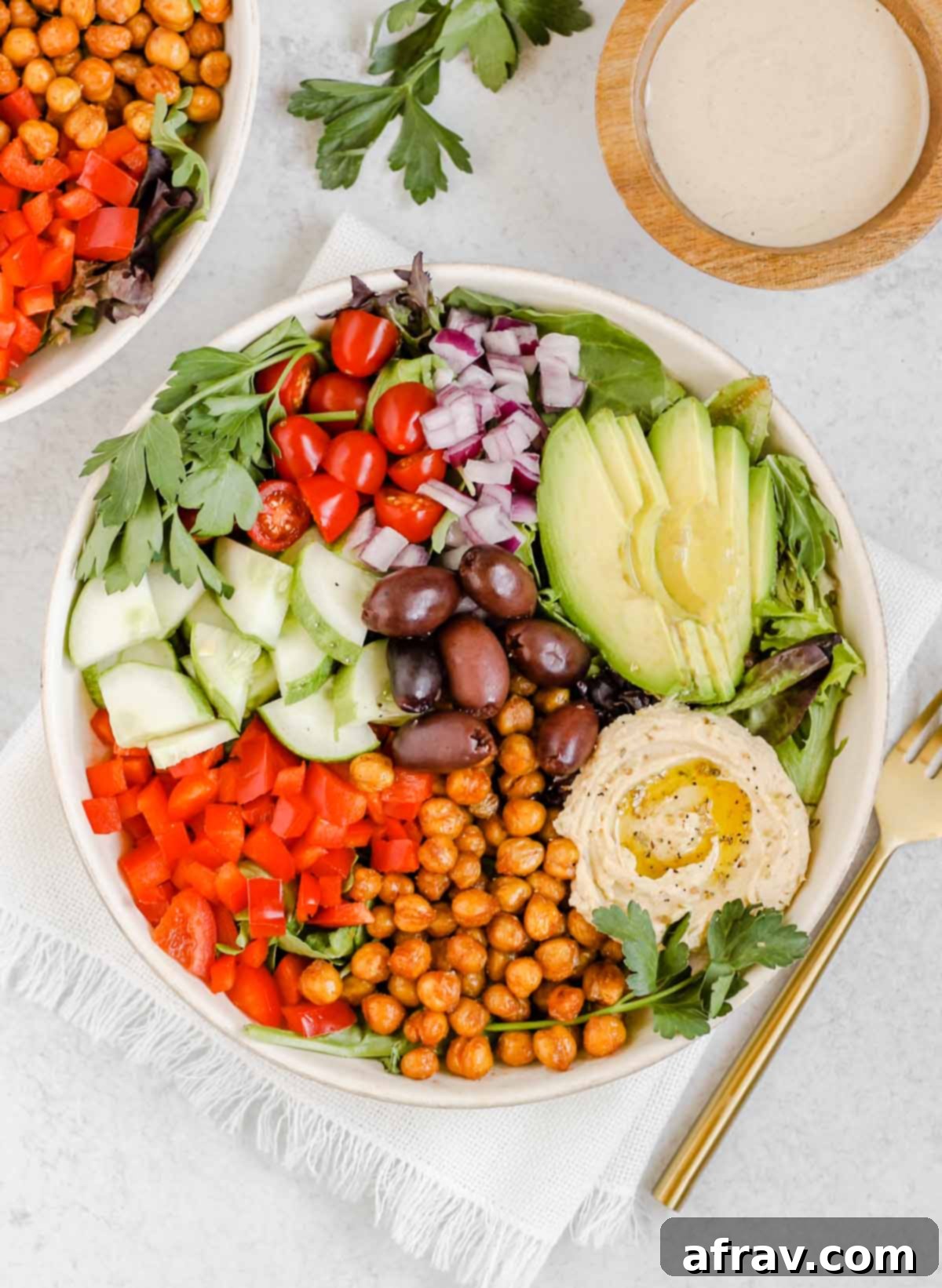 Mediterranean salad in a white bowl with a gold fork and a side of tahini dressing. 