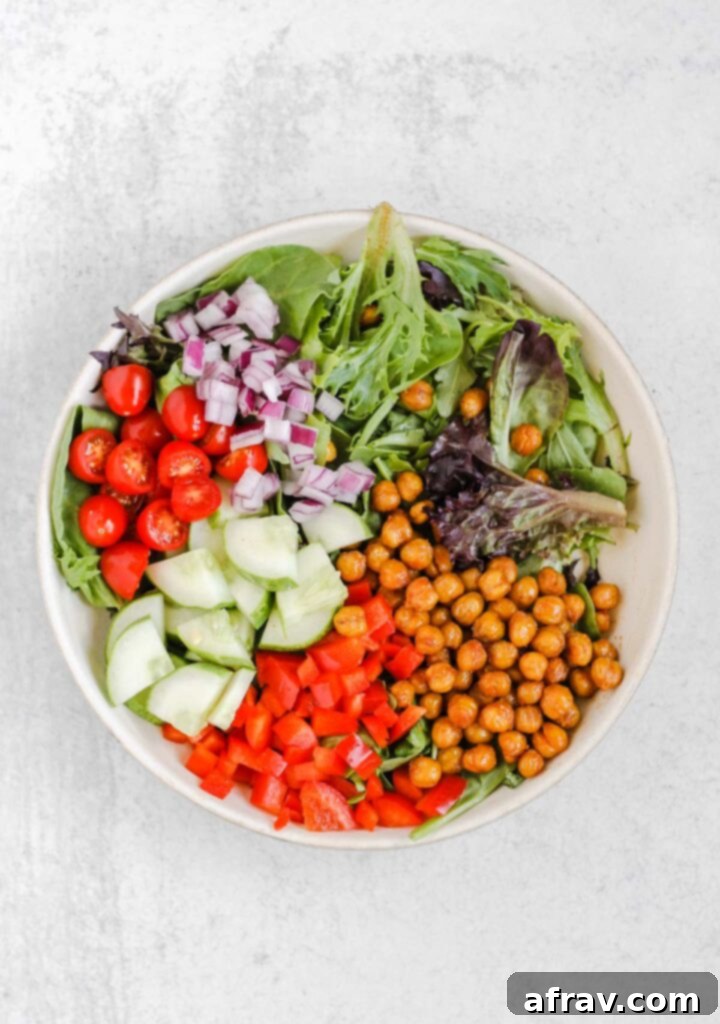 Mixed greens, roasted chickpeas, peppers, cucumbers, tomatoes, and onions in a salad bowl. 