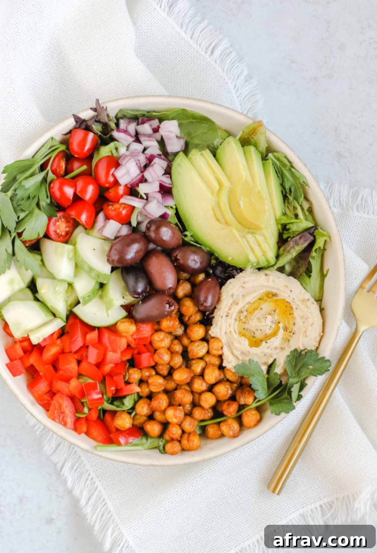 Mediterranean salad in a white bowl with a gold fork.