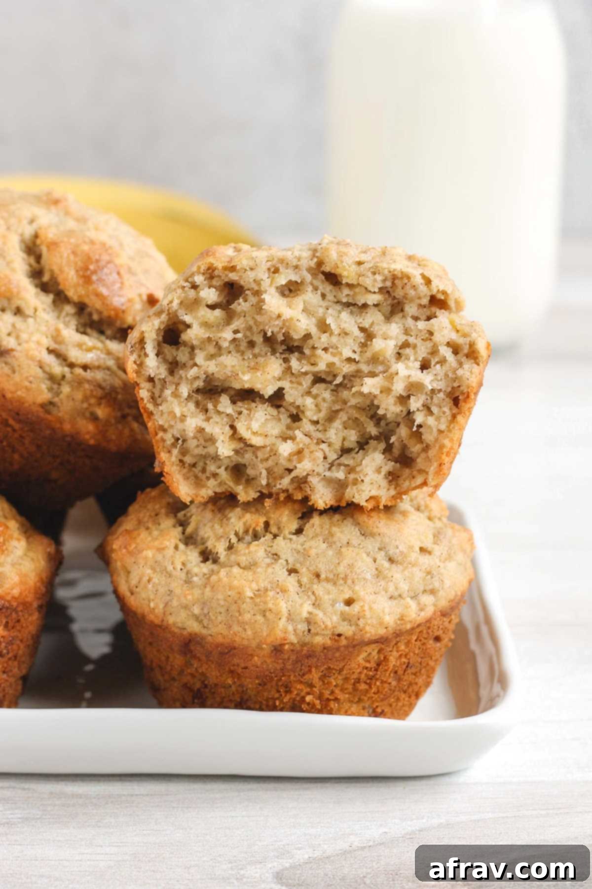 Banana muffins stacked 2 high with top one cut open to show texture.