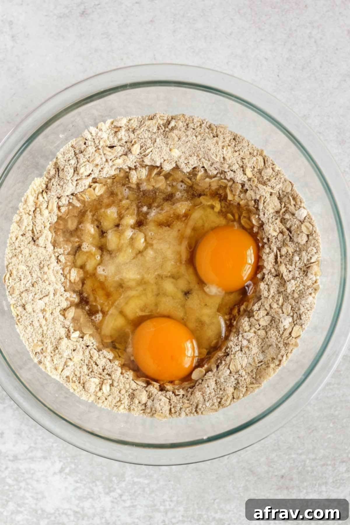 Gluten Free Banana Dream Muffins 5 Dry ingredients for gluten-free banana muffins in a glass mixing bowl with all wet ingredients (eggs, oil, maple syrup, mashed bananas) freshly added to the center well.