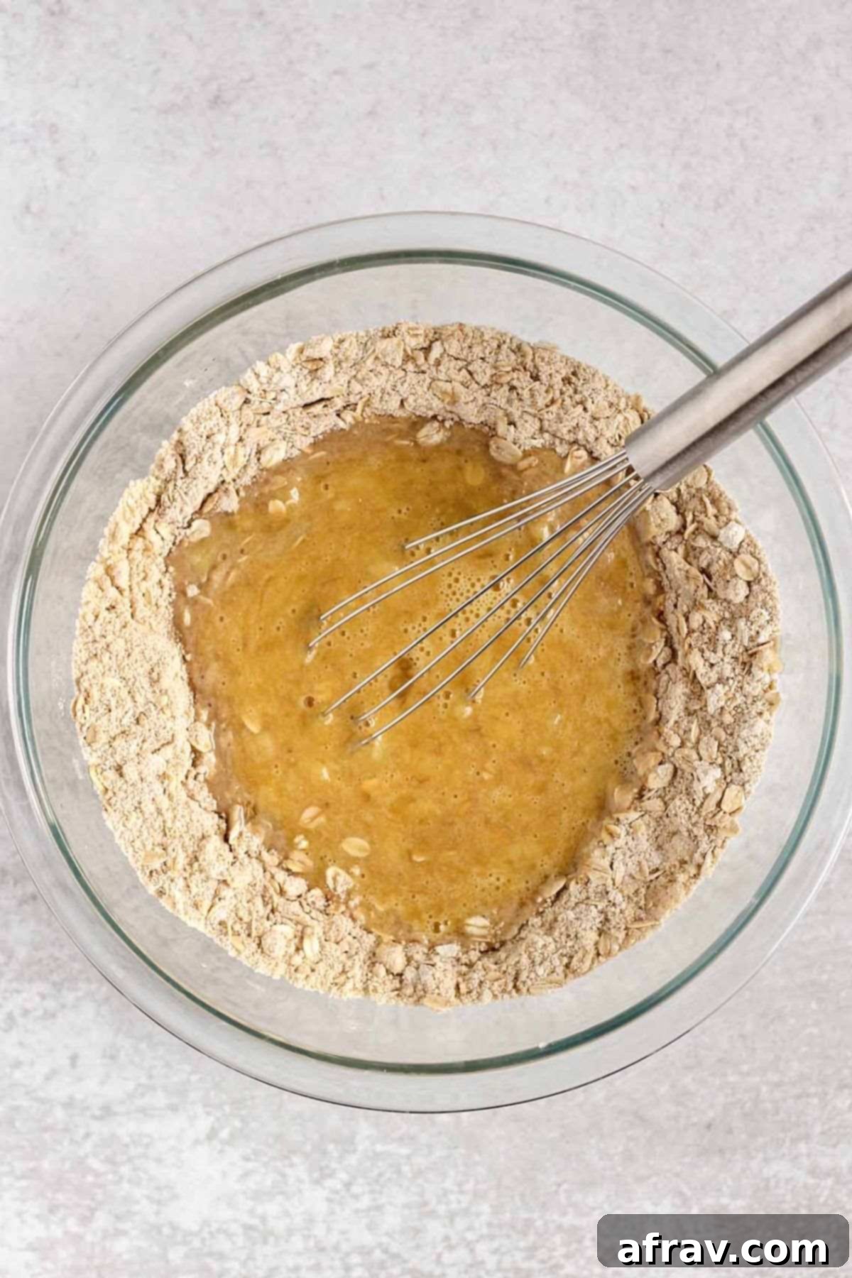 Wet ingredients in the center of dry ingredients with a whisk in a glass mixing bowl.
