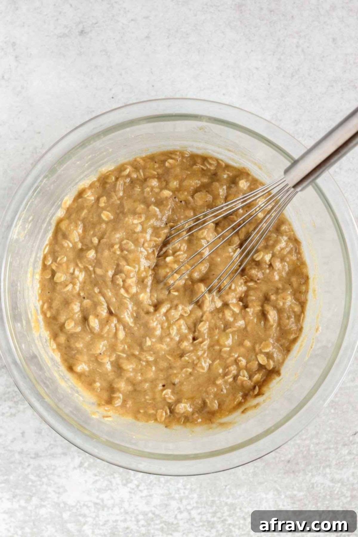 Banana muffin batter with a wire whisk in a glass mixing bowl.