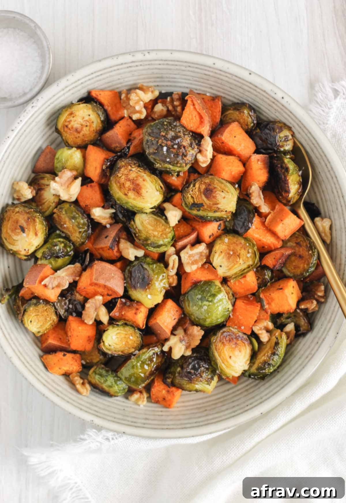 Roasted sweet potatoes and Brussels sprouts in a serving bowl with a gold spoon.