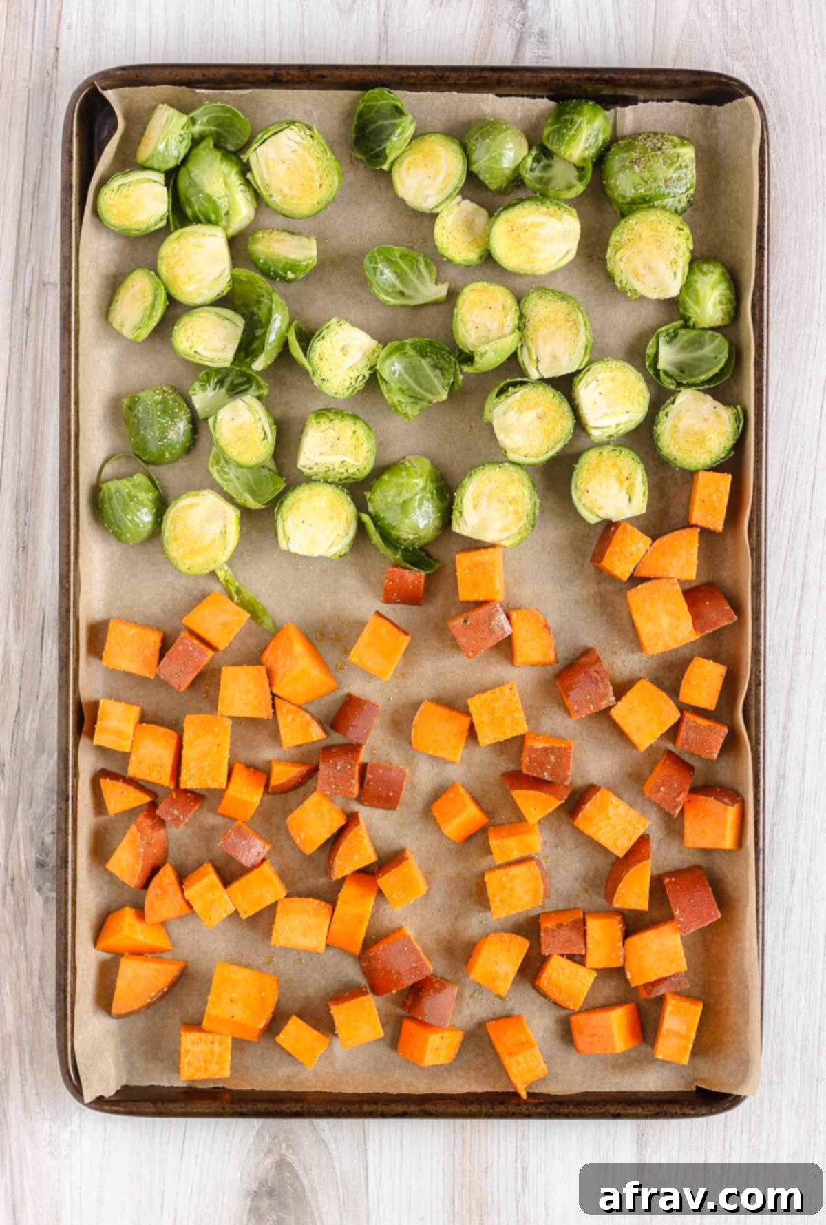 Raw Brussels sprouts and cubed sweet potatoes on a baking sheet.