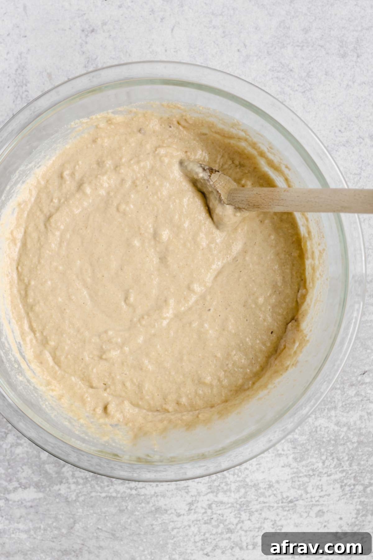 Gluten-free waffle batter in a glass mixing bowl with a wooden spoon.