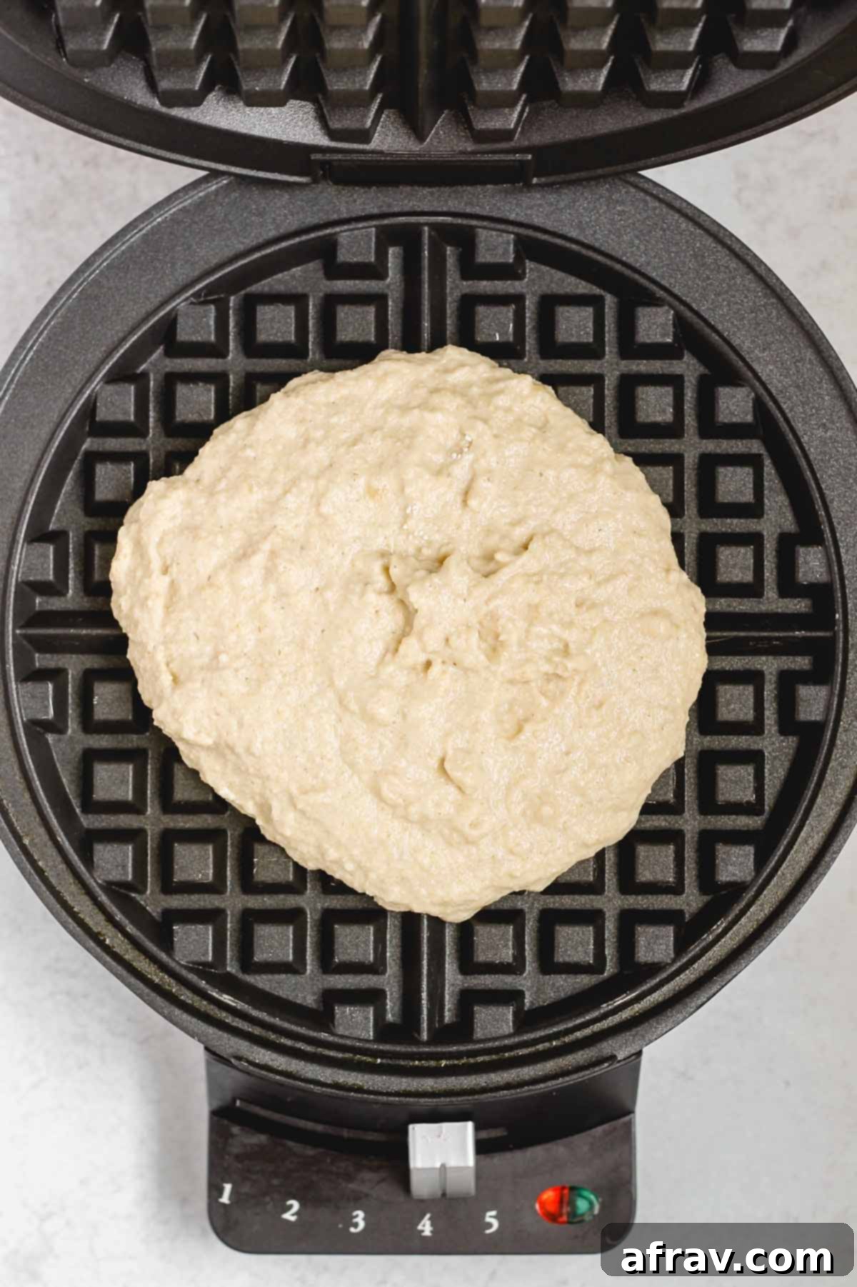 Deliciously Free Waffles 6 Freshly poured gluten-free waffle batter settling into the hot plates of a waffle iron, just before closing to cook.