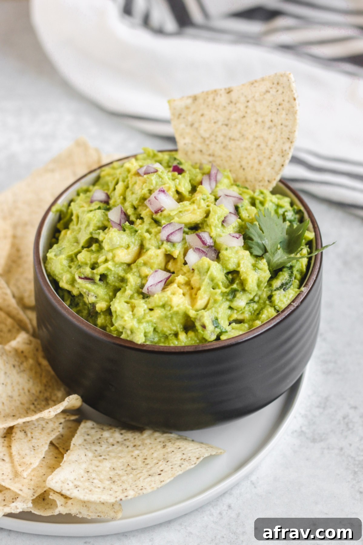 side view of guacamole in a black bowl with a chip sticking out of the quacamole