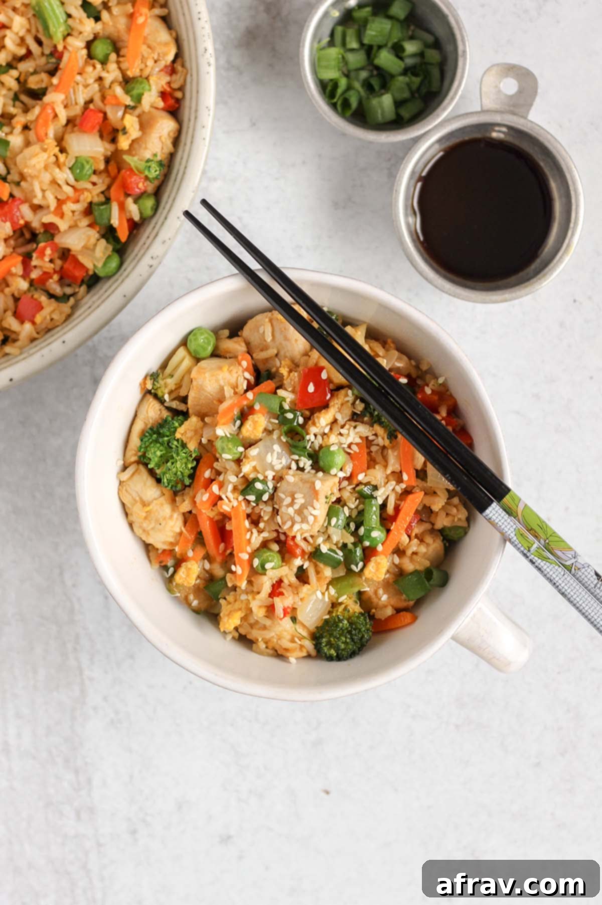 Chicken fried rice with lots of veggies in a single serve dish with chopsticks laid on top.