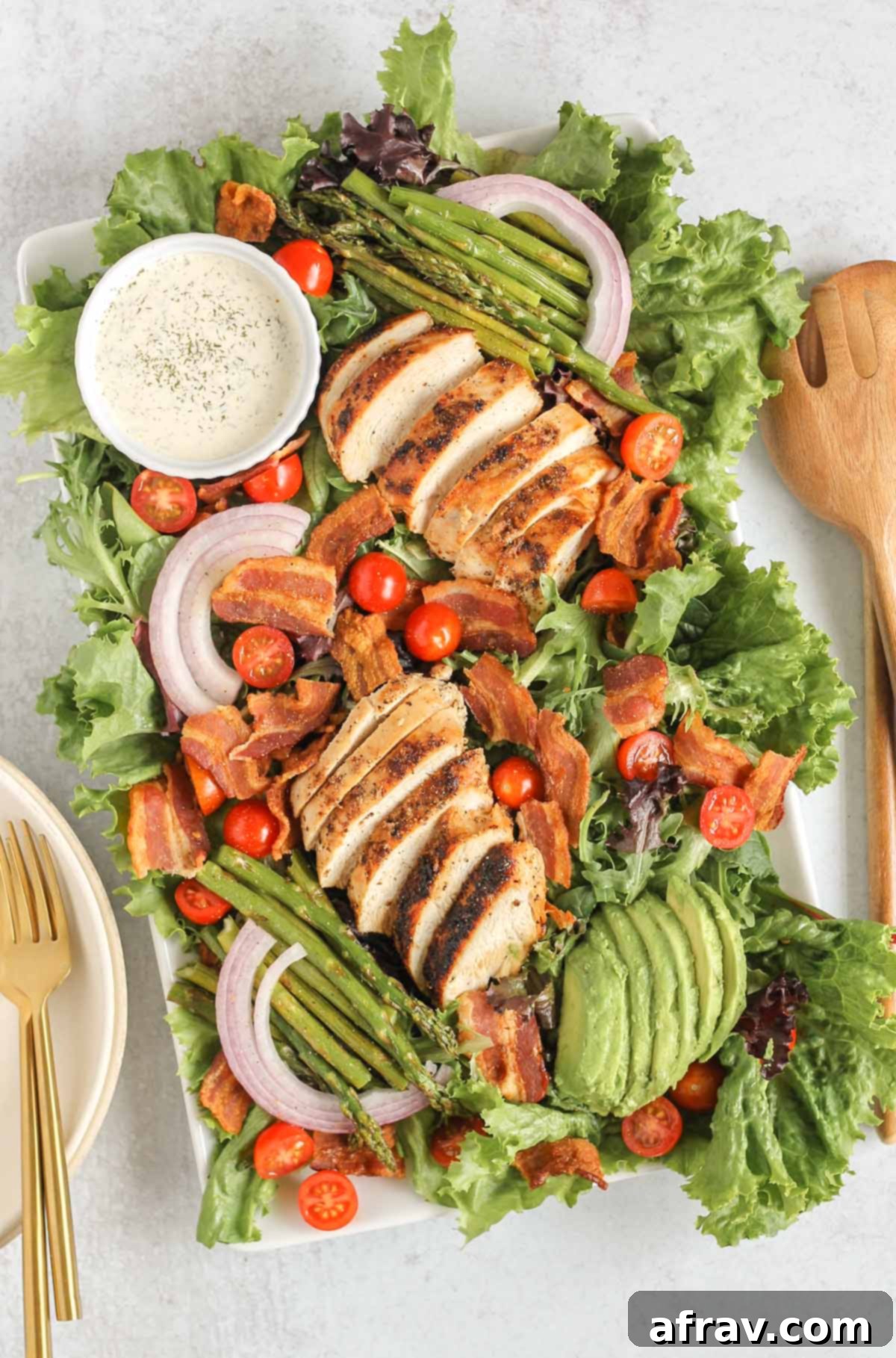 BLT Bliss Chicken Salad 2 Large serving tray featuring a colorful BLT chicken salad, brimming with grilled chicken, crispy bacon, ripe avocado slices, fresh cherry tomatoes, and roasted asparagus, accompanied by a small ramekin of creamy dairy-free ranch dressing.