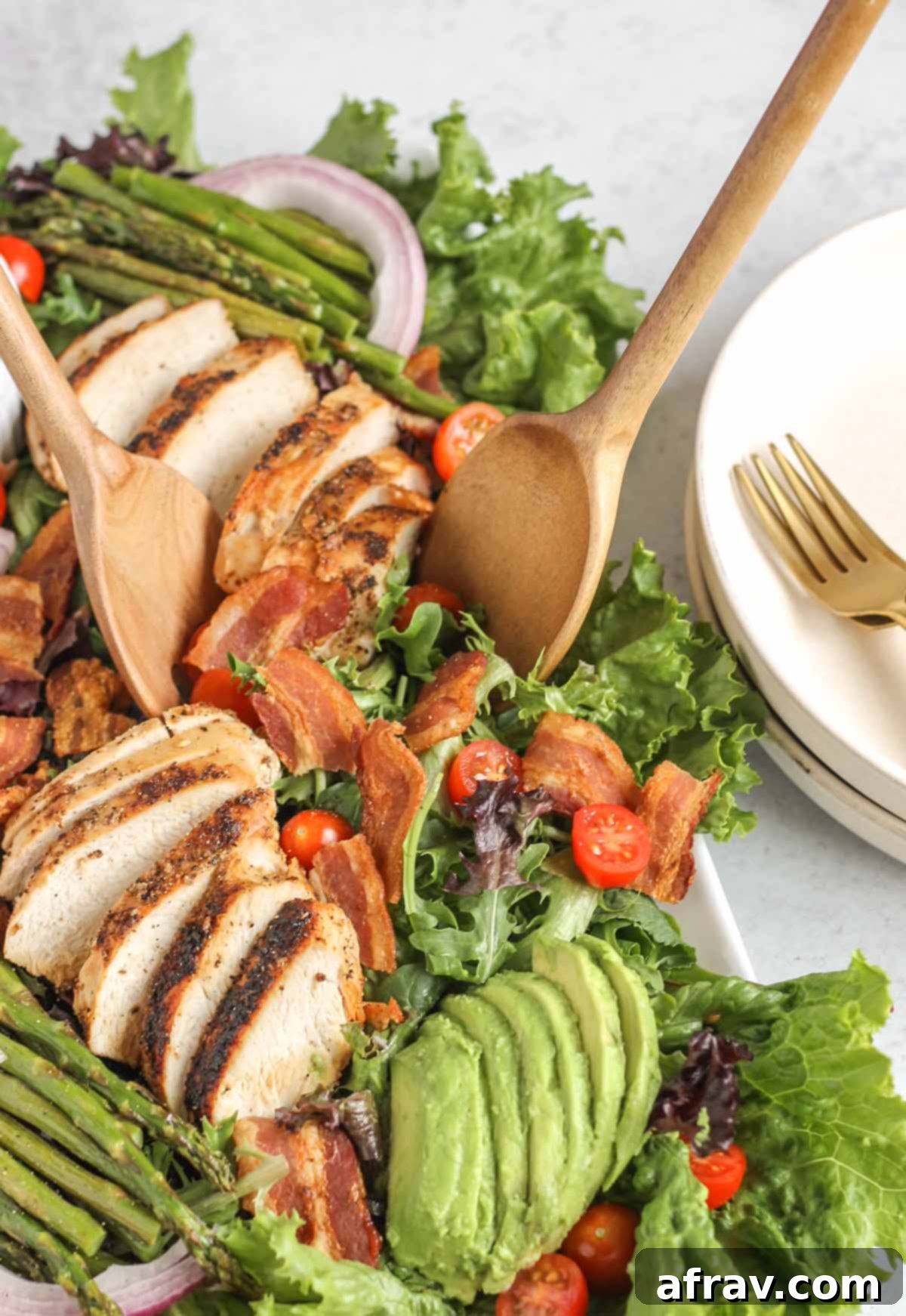 BLT Bliss Chicken Salad 5 Two rustic wooden salad utensils scooping a generous portion of BLT chicken salad, rich with chicken, bacon, avocado, and asparagus, from a large serving tray.