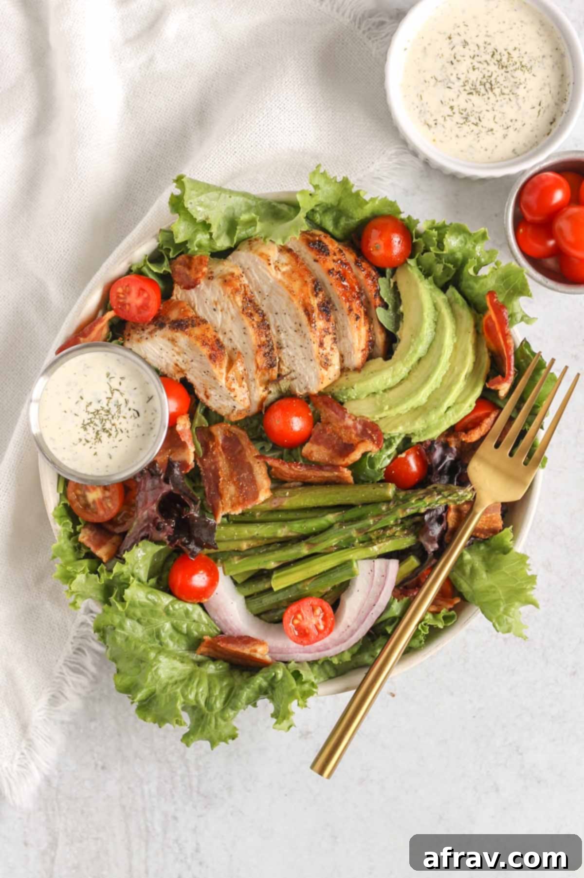 BLT Bliss Chicken Salad 6 A perfectly portioned salad bowl filled with healthy BLT chicken salad, featuring generous amounts of chicken, crispy bacon, avocado slices, roasted asparagus, and cherry tomatoes, with a side of creamy ranch dressing.