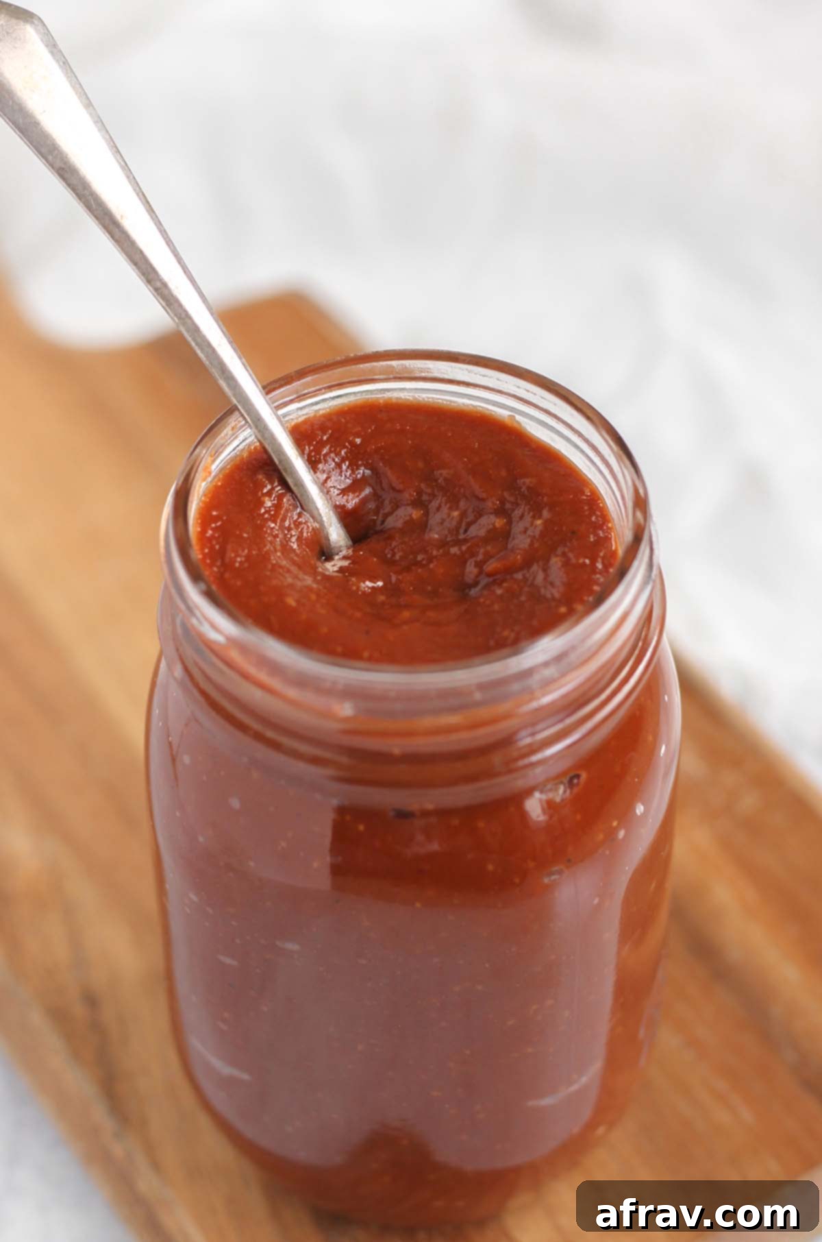 Delicious Whole30 Paleo BBQ Sauce 8 Mason jar of Whole30 BBQ sauce with a spoon dipped in it, showcasing its rich texture.