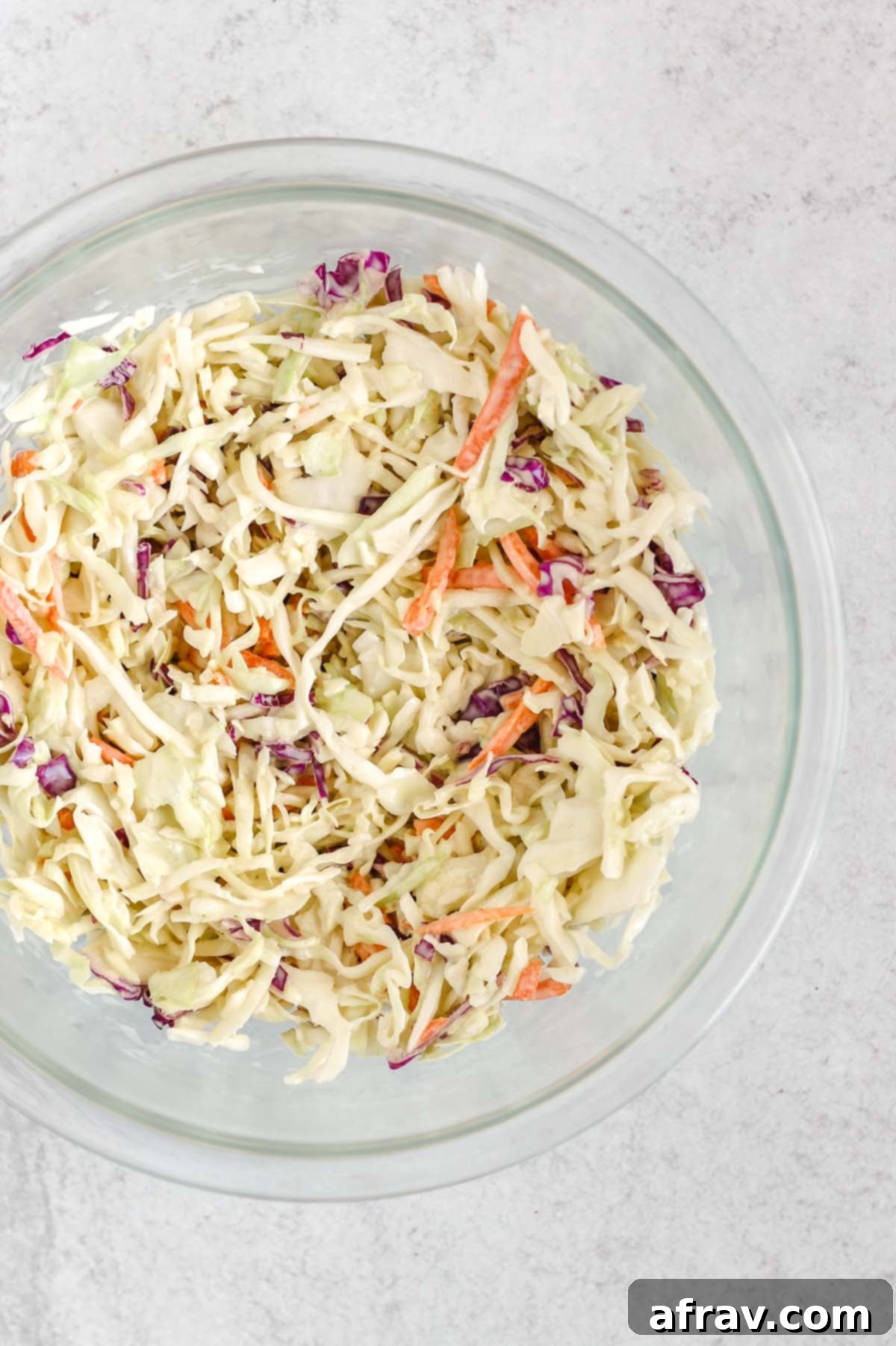 Coleslaw mixed with dressing in a mixing bowl, showing the perfectly coated vegetables.