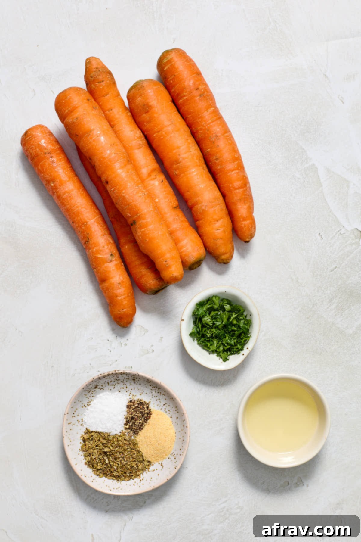 Individual ingredients neatly arranged for air fryer carrots, including fresh carrots, olive oil, dried Italian seasoning, garlic powder, salt, and pepper.