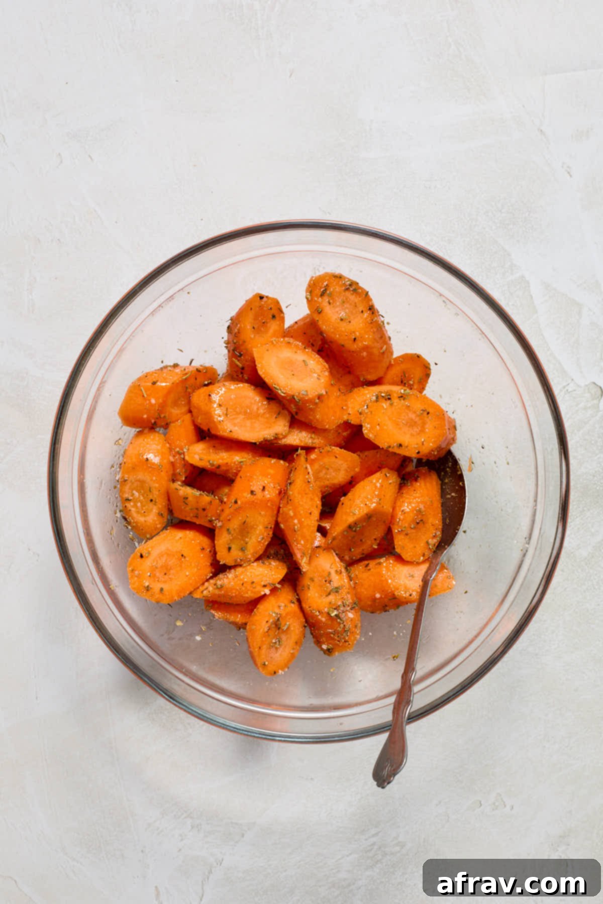 Sliced carrots in a glass bowl, evenly coated with olive oil and seasonings after tossing.