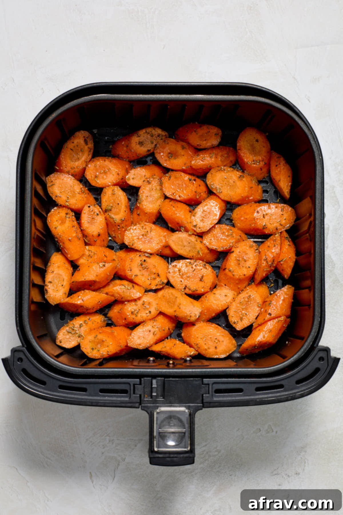 Seasoned carrot pieces arranged in a single layer inside an air fryer basket.
