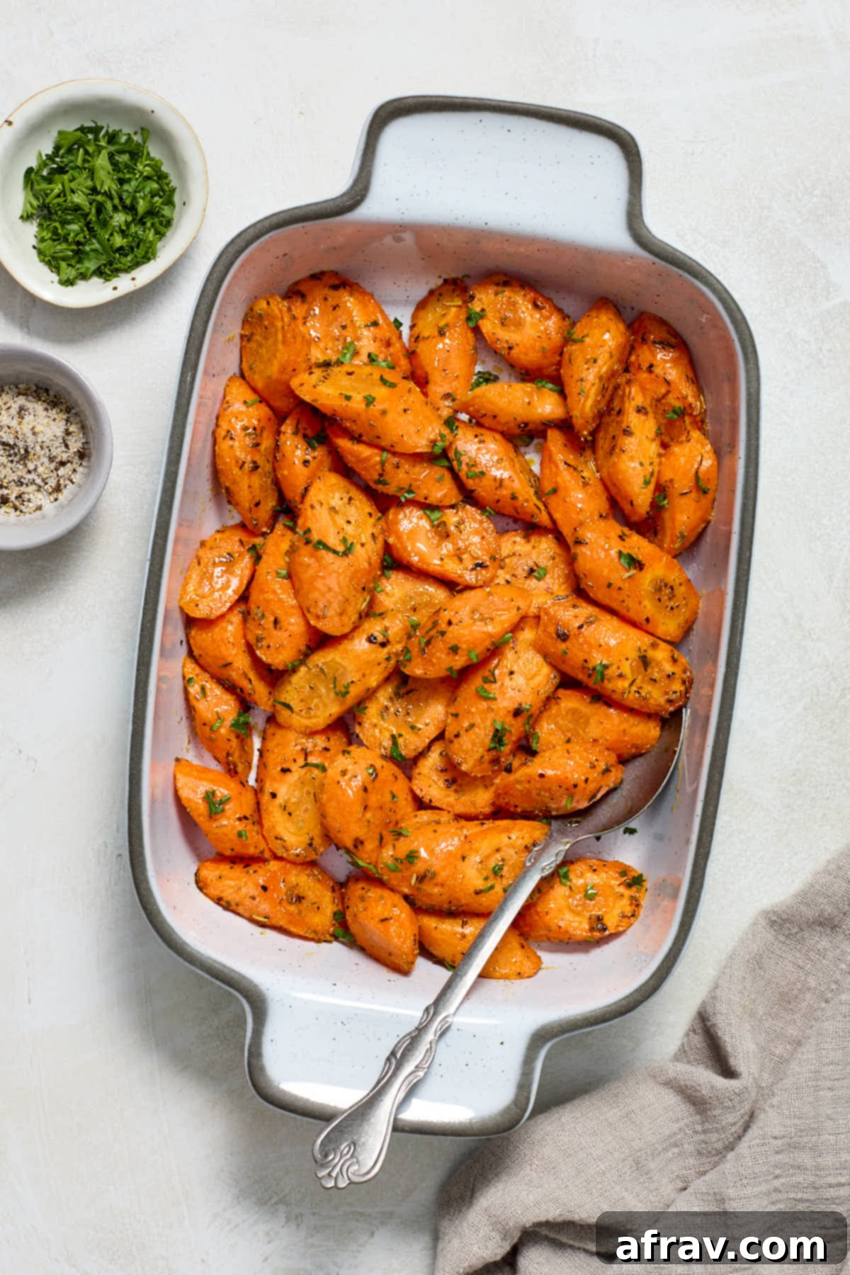 Beautifully roasted air fried carrots arranged in a white serving dish, with small bowls of fresh herbs, salt, and pepper on the side.