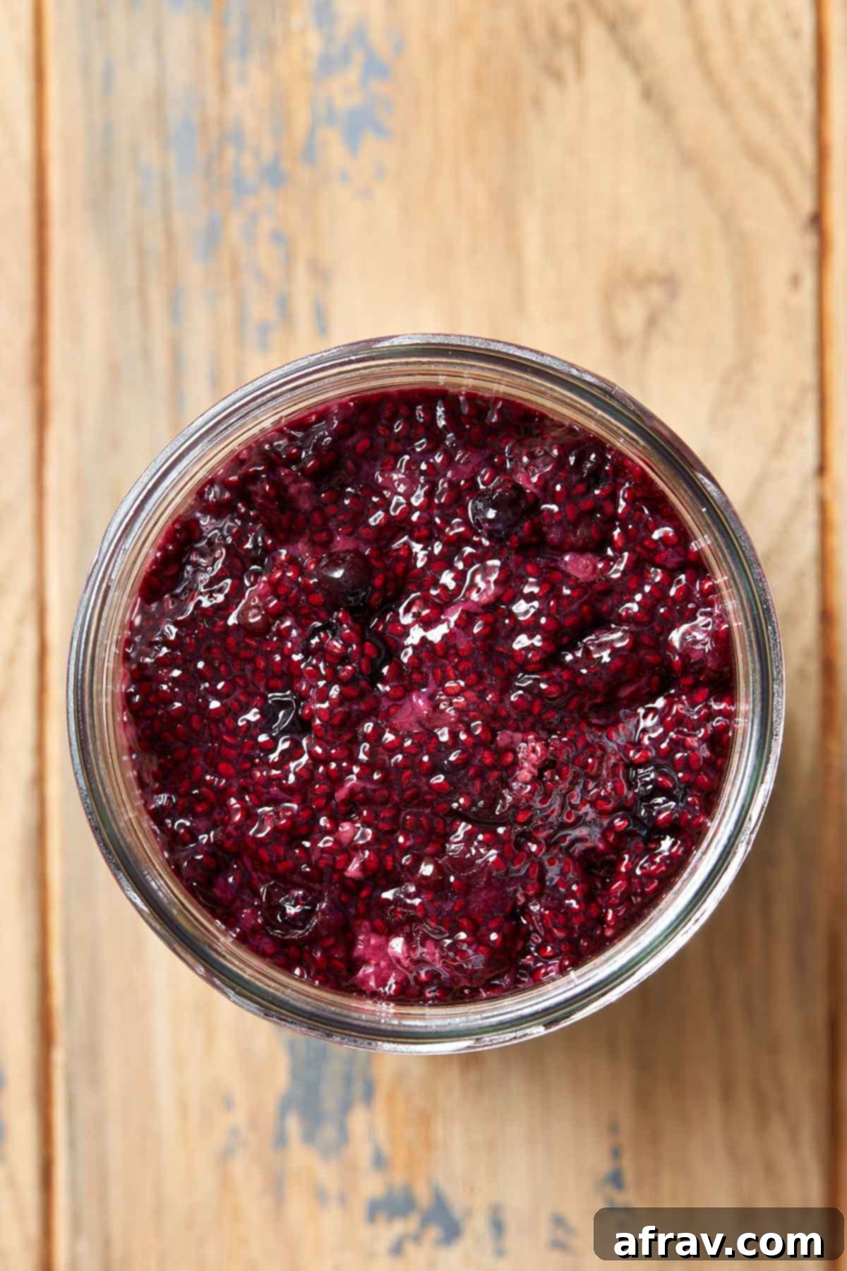 Overhead view of homemade triple berry chia seed jam in a clear glass jar on a rustic wooden table, surrounded by fresh berries.