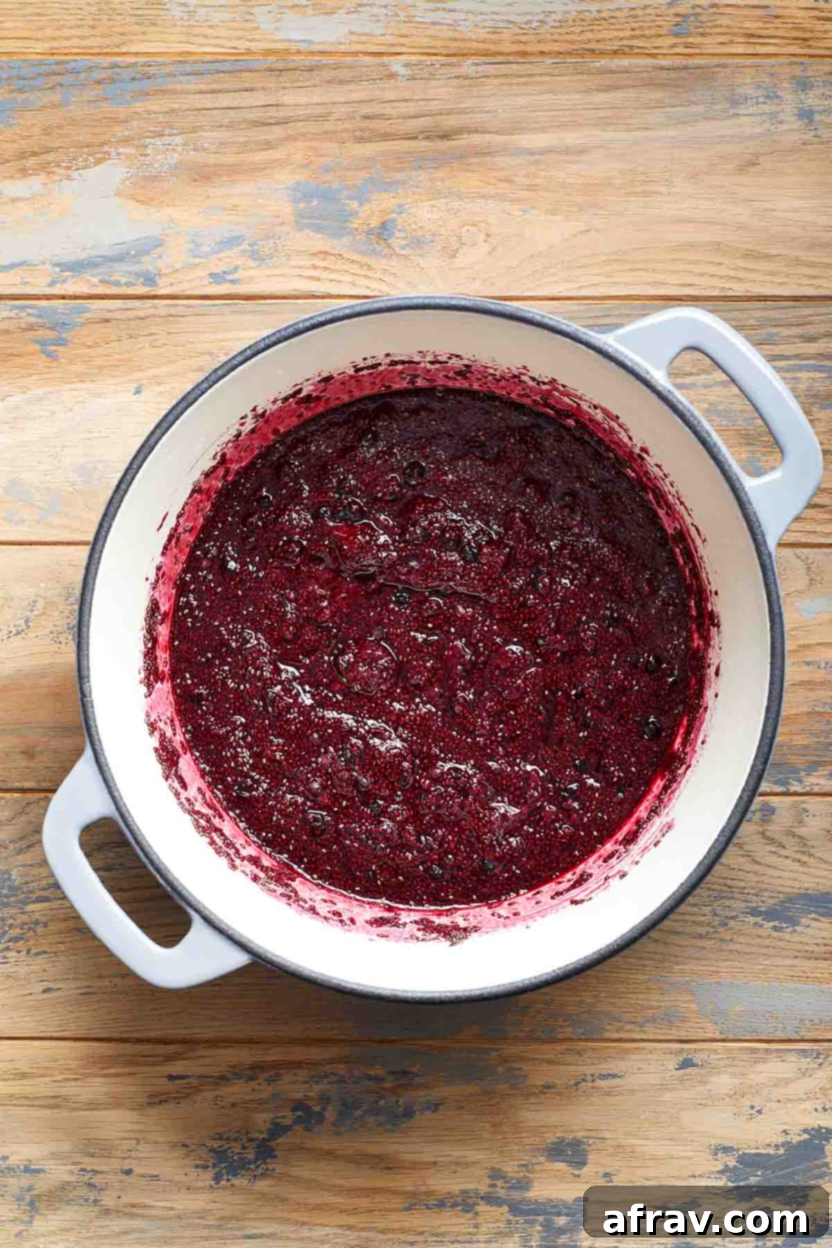 Mashed berries mixed with chia seeds in a pot, beginning to thicken.