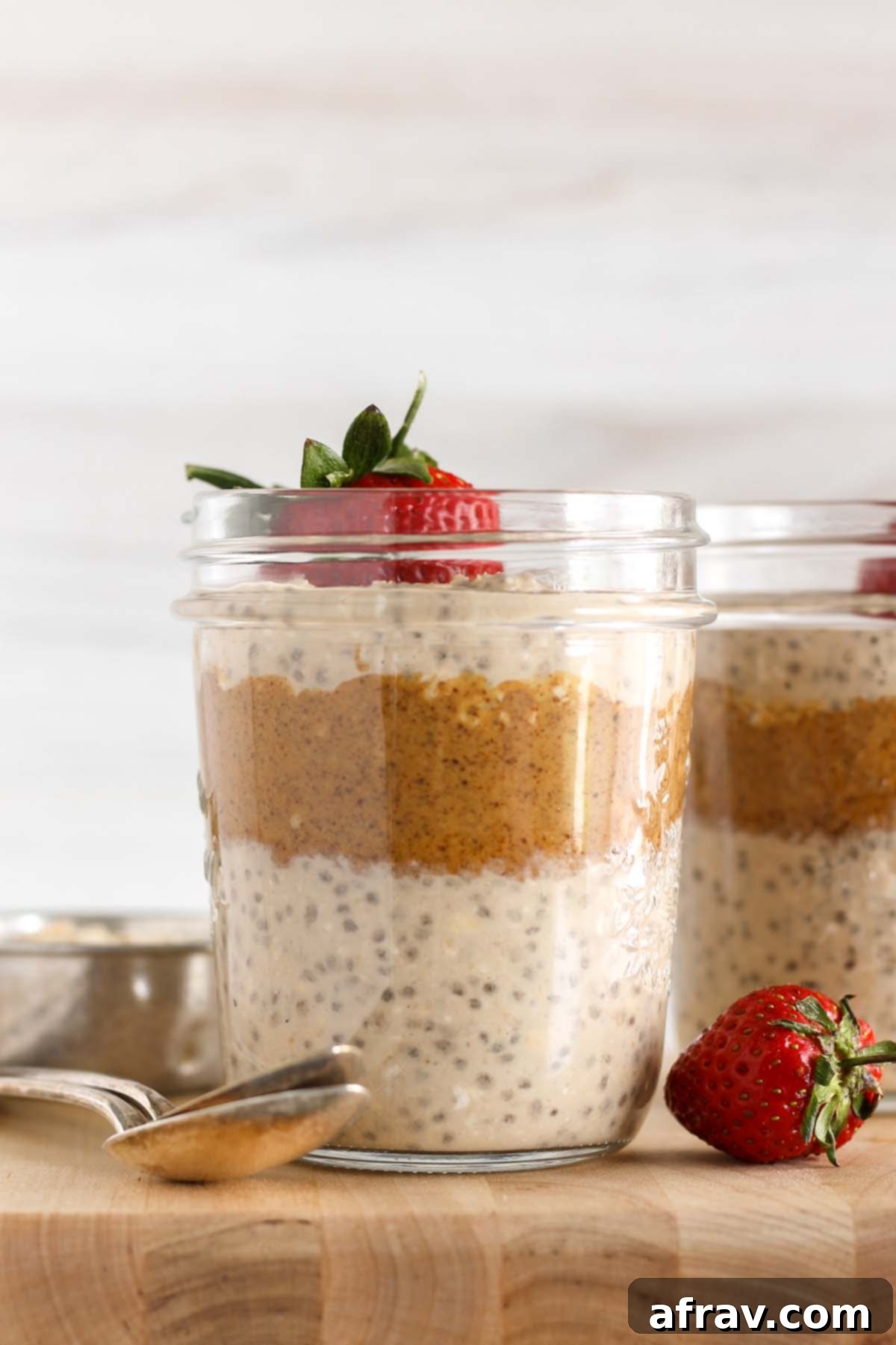 Mason jar filled with layers of overnight oats and almond butter topped with a strawberry.