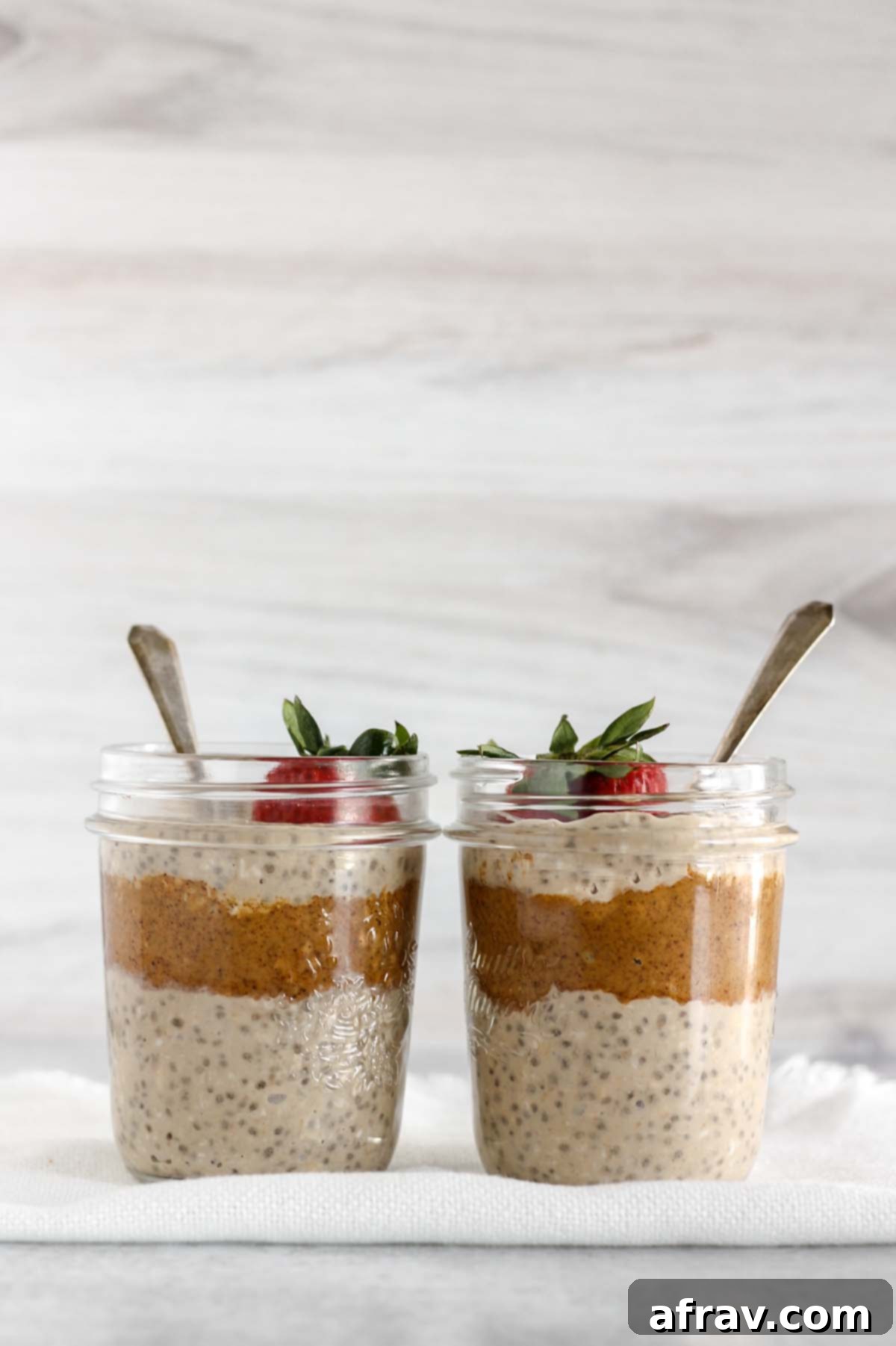 Two mason jars filled with overnight oats and almond butter topped with a strawberry.