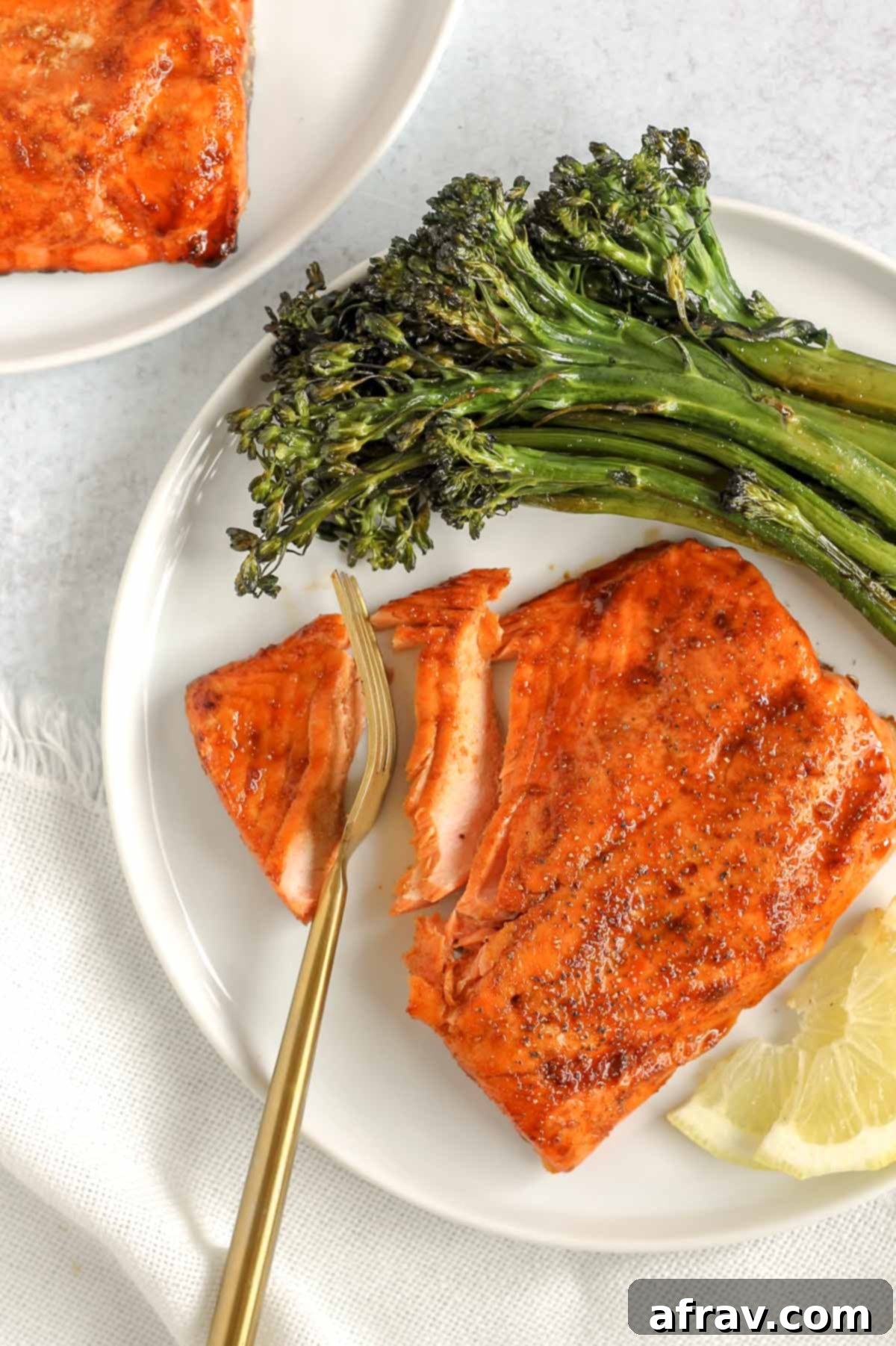 A gold fork cutting into a salmon fillet on a plate with broccolini.