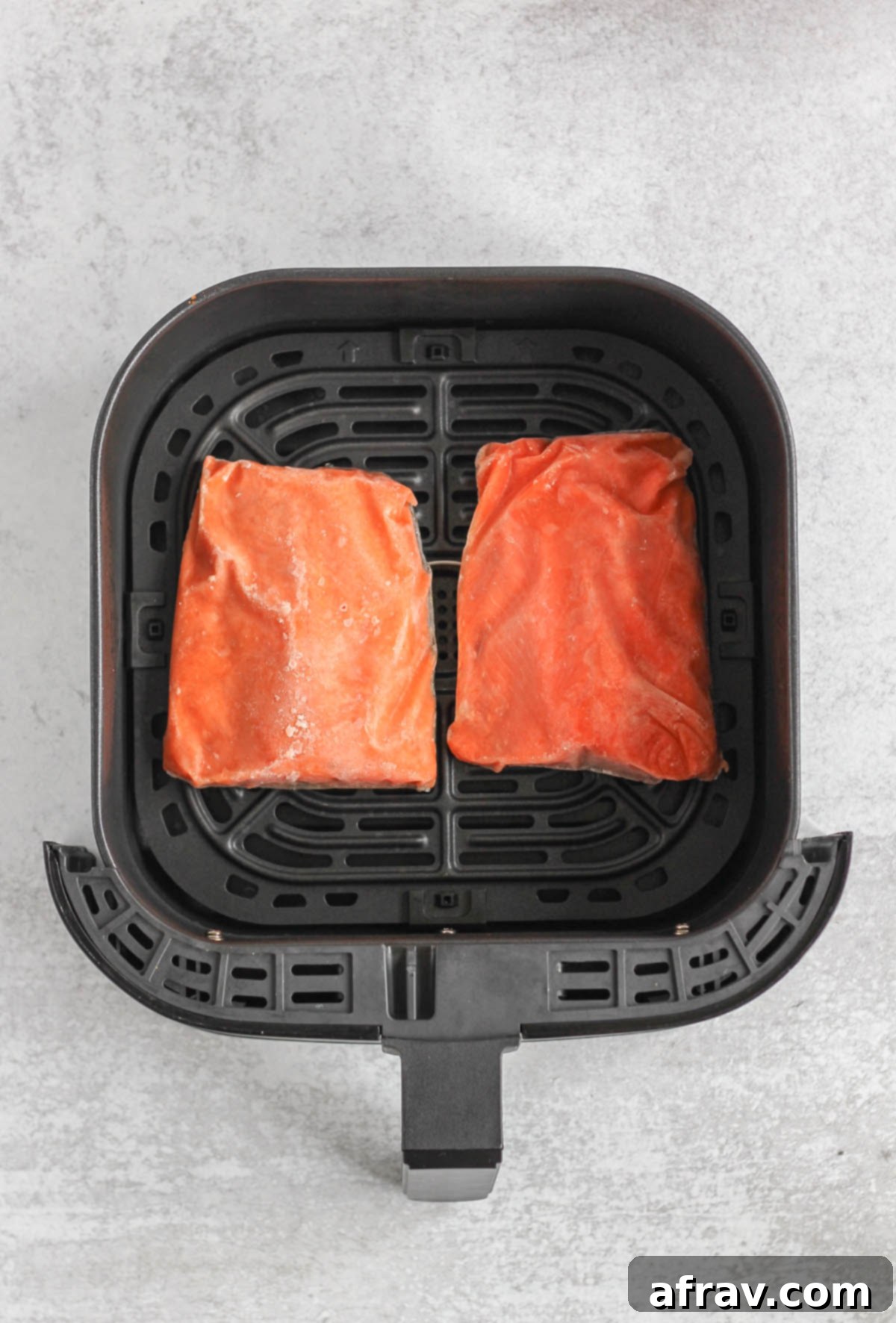 Frozen salmon fillets in an air fryer basket.