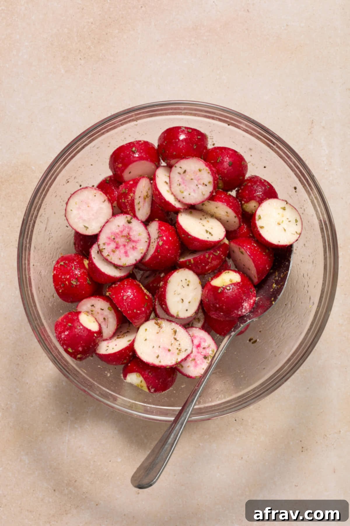 Radishes tossed with oil and seasonings in a glass bowl.