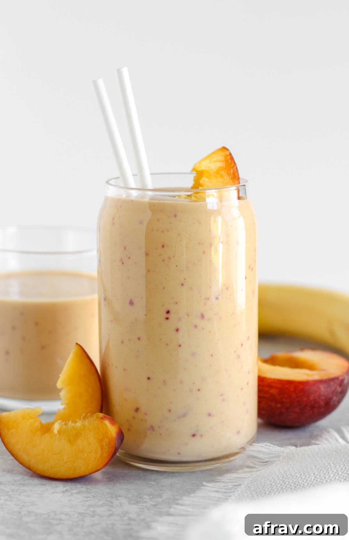 Tall glass filled with peach smoothie with sliced peaches leaning up against the glass.