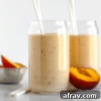 Two glasses filled with peach smoothie with half a peach laying next to the glasses.