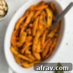Up close and overhead view of golden brown air fryer pumpkin fries in a white dish with a fork inserted into it, highlighting their perfect texture.