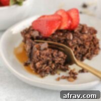 Gold fork cutting a bite off of a piece of chocolate baked oats topped with strawberries.
