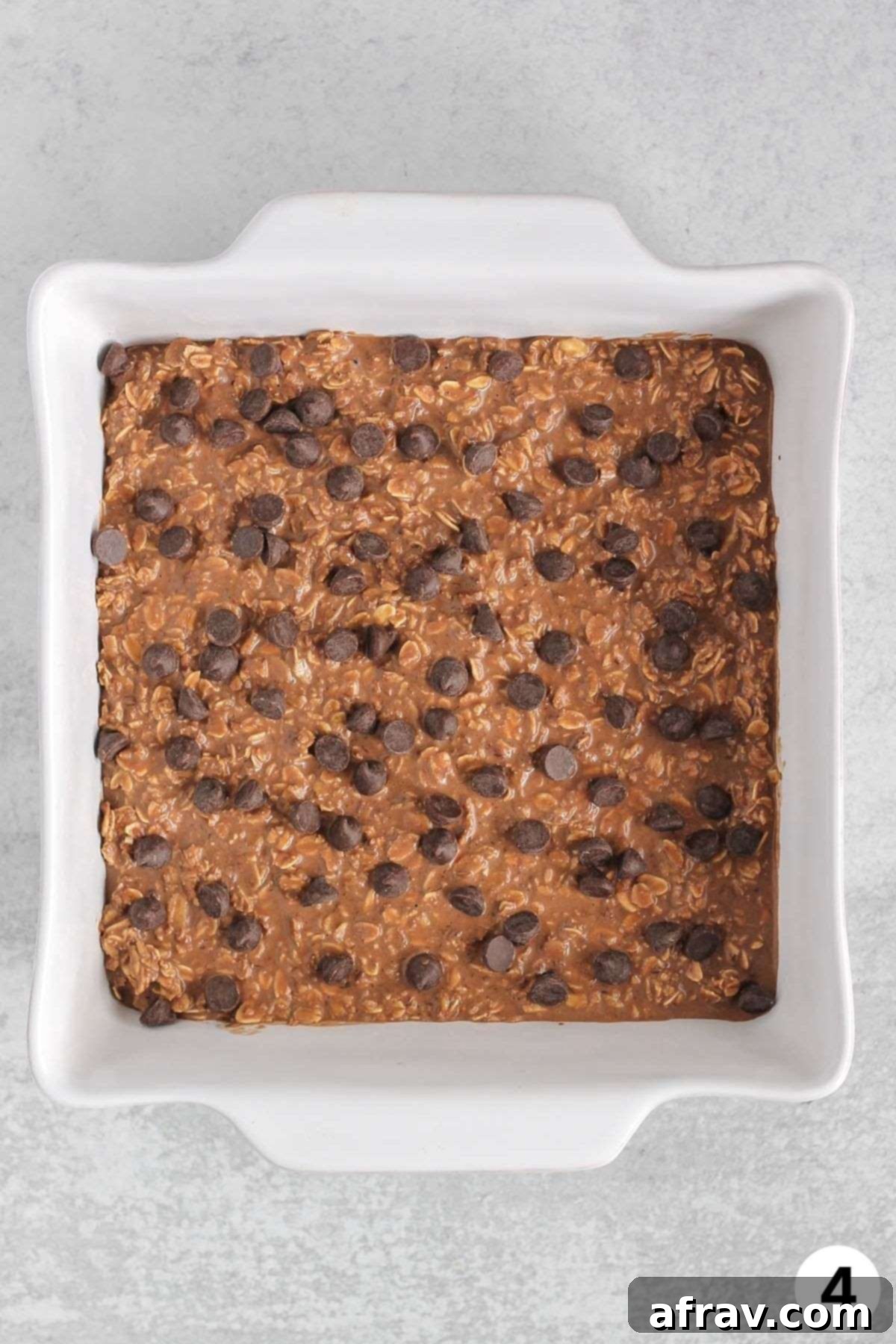 Chocolate baked oats mixture topped with chocolate chips in a baking pan before being baked.