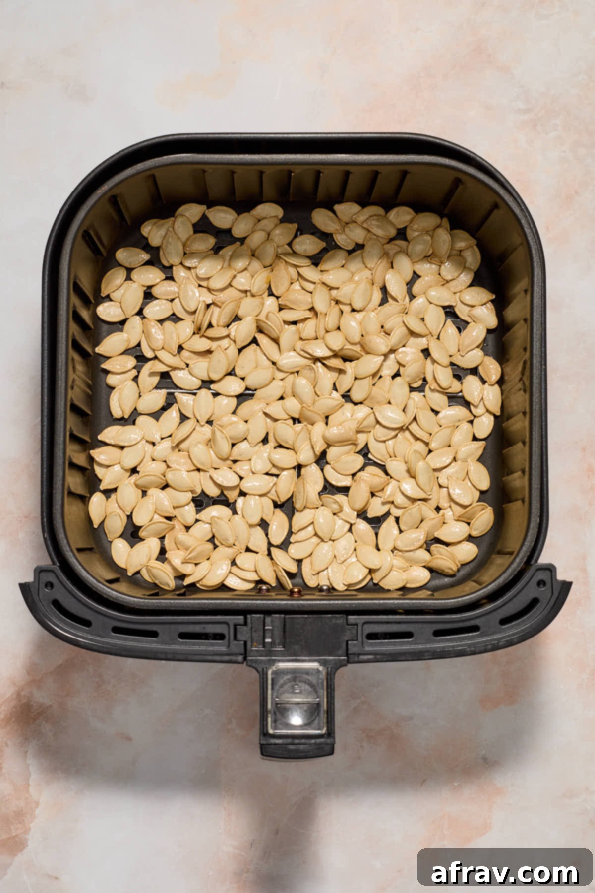 Seasoned pumpkin seeds arranged in a single, thin layer in an air fryer basket, ready for cooking.