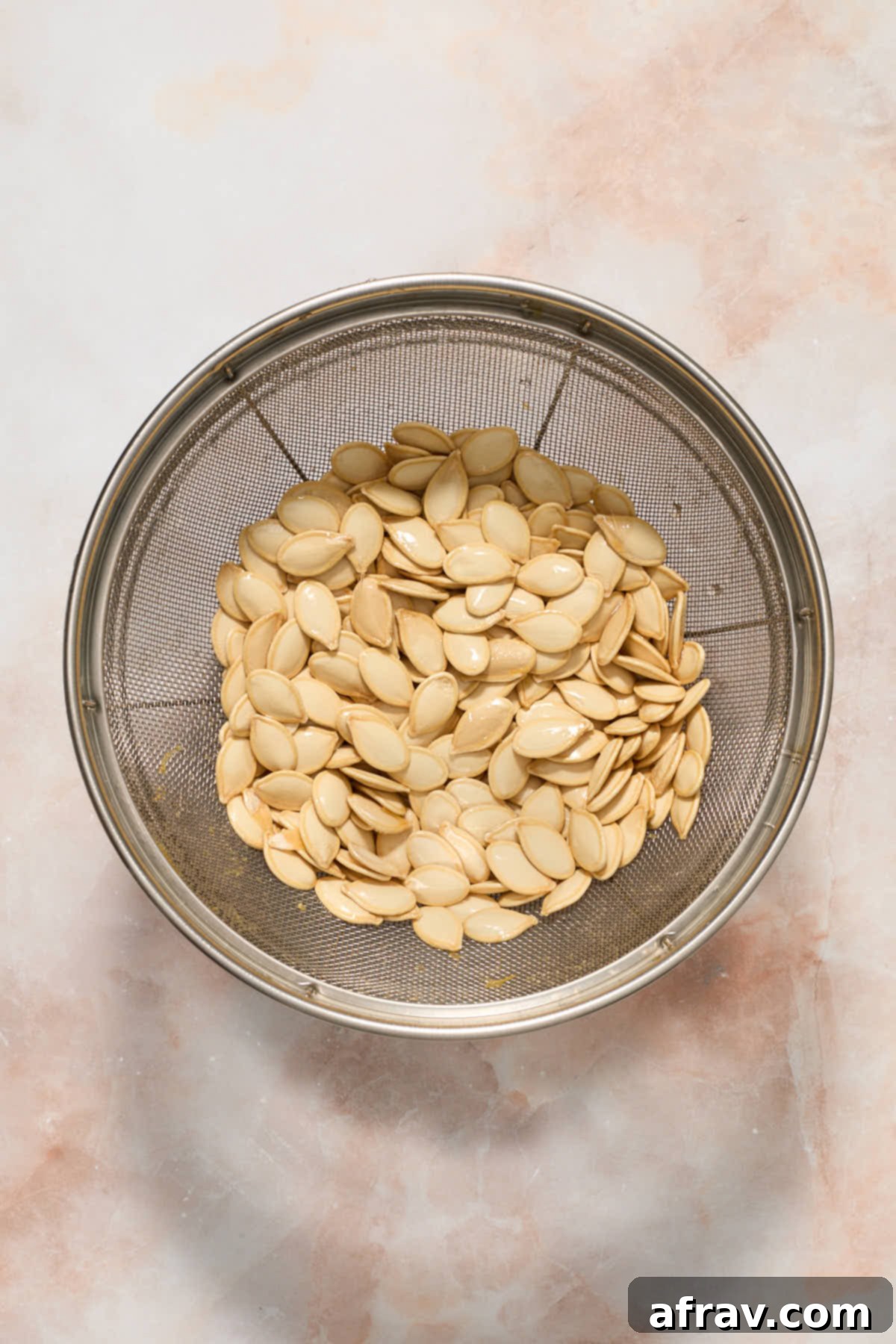 Clean pumpkin seeds draining in a colander under running water.