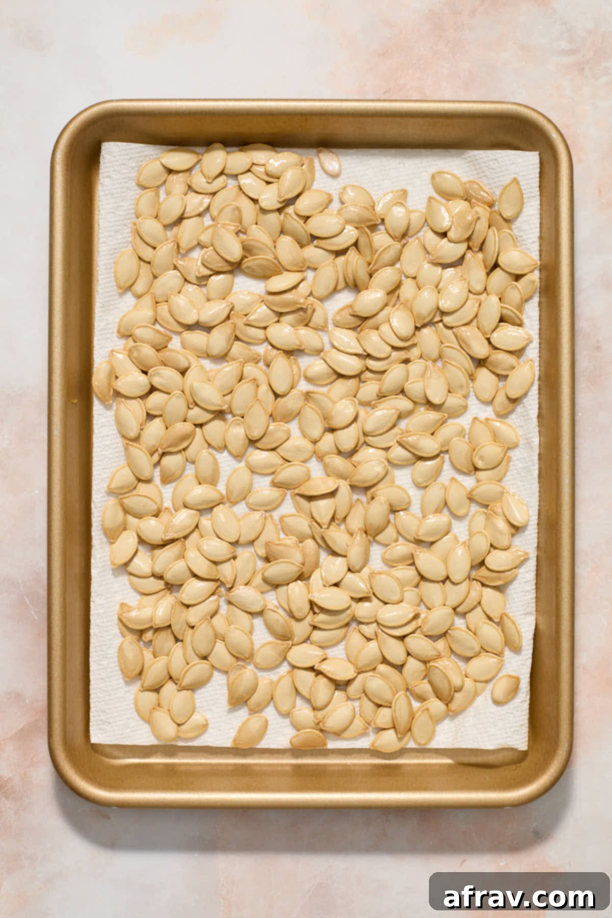 Clean pumpkin seeds spread out on a paper towel-lined tray to air dry.
