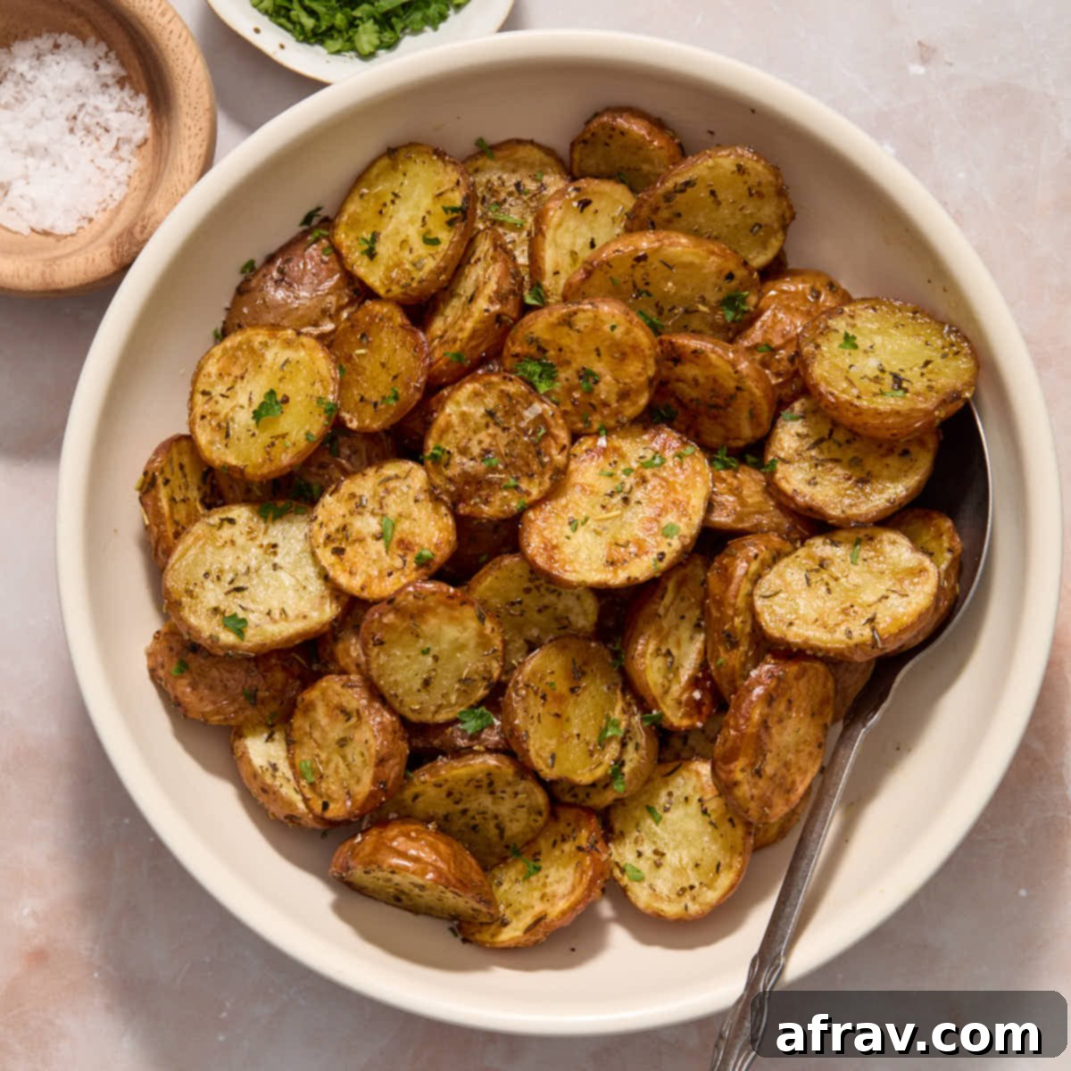 Effortless Air Fryer Side Dishes 11 Air fryer baby potatoes served in a white bowl and topped with sea salt and chopped fresh parsley, looking perfectly roasted.