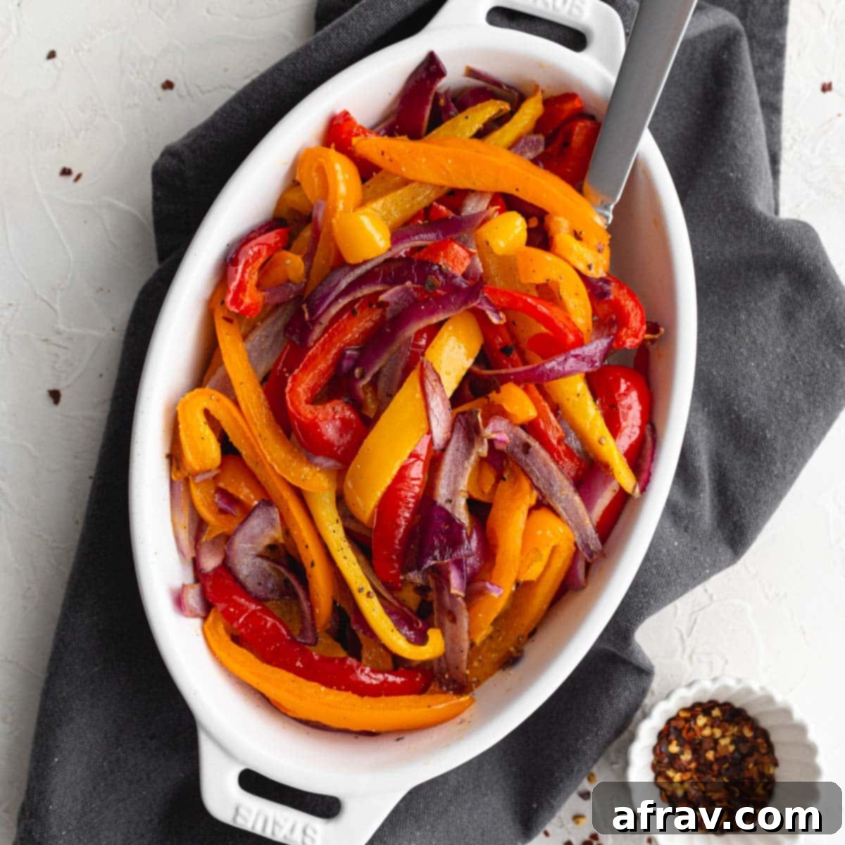 Effortless Air Fryer Side Dishes 12 Air fried mixed bell peppers and red onions served in a white dish with a spoon, showing vibrant colors and tender texture.
