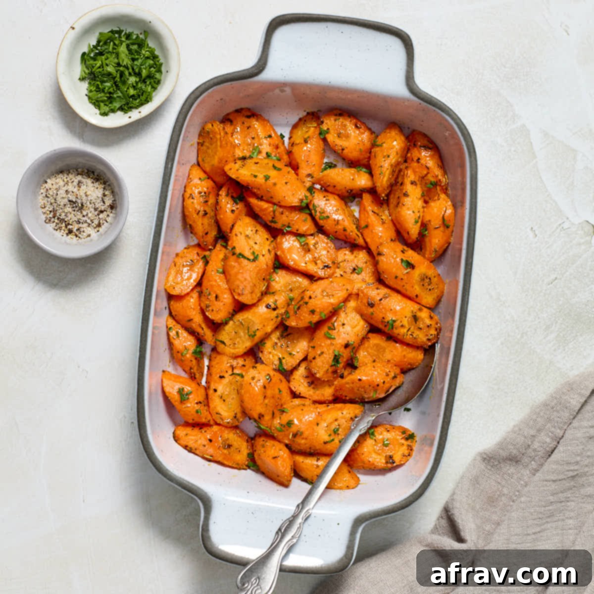 Effortless Air Fryer Side Dishes 3 Air fryer carrots served in a white dish with fresh parsley and salt and pepper on the side, highlighting their vibrant color and fresh appeal.